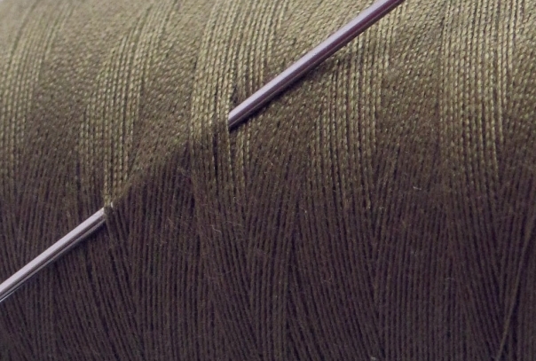Close-up of a sewing needle stuck through a layer of threads on a roll of sewing thread